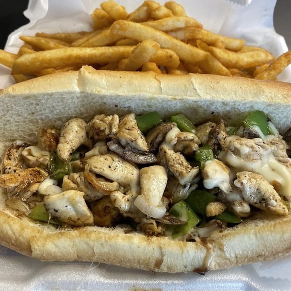 A chicken cheesesteak sandwich with green peppers, onions, and melted cheese, served with fries.