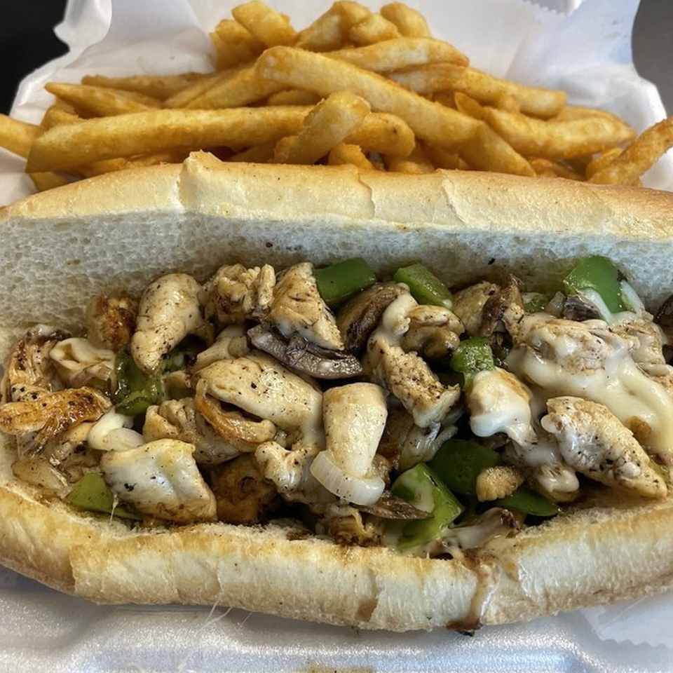 A chicken cheesesteak sandwich with green peppers, onions, and melted cheese, served with fries.