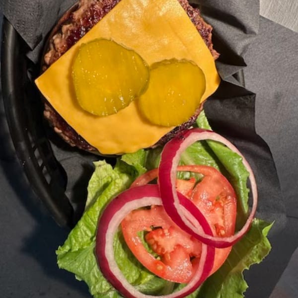 A Peppajak burger with cheese, pickles, lettuce, tomato, and red onion, served in a basket.