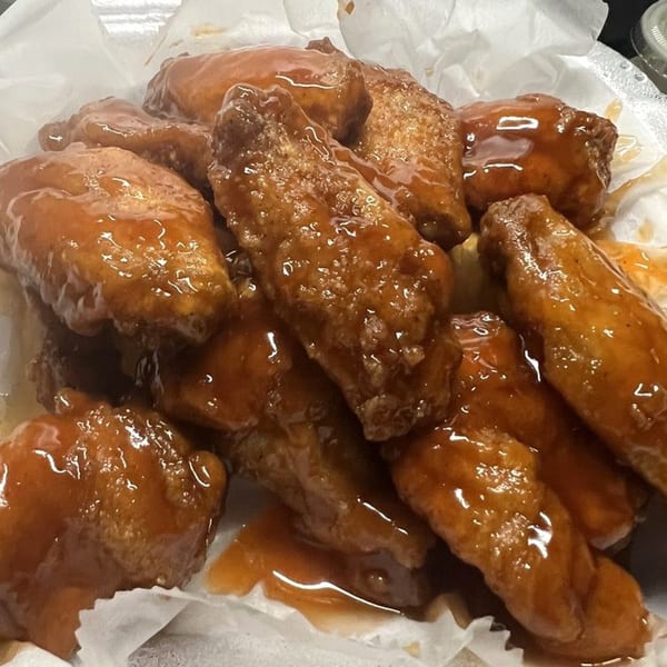 Close-up of Peppajak's sticky, saucy chicken wings in a white paper container.
